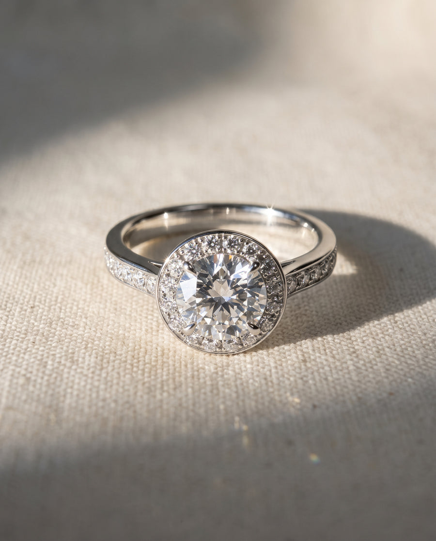 Round diamond halo engagement ring in silver-toned metal with pavé-set diamonds on the band.
