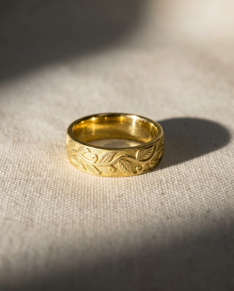 5mm 9ct yellow gold wedding ring featuring an intricate engraved leaf motif on a textured surface.
