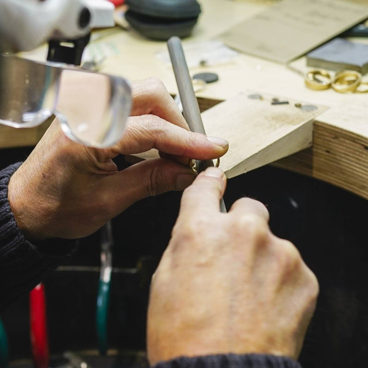 Hands filing a ring on a jeweller’s bench using a hand tool.
