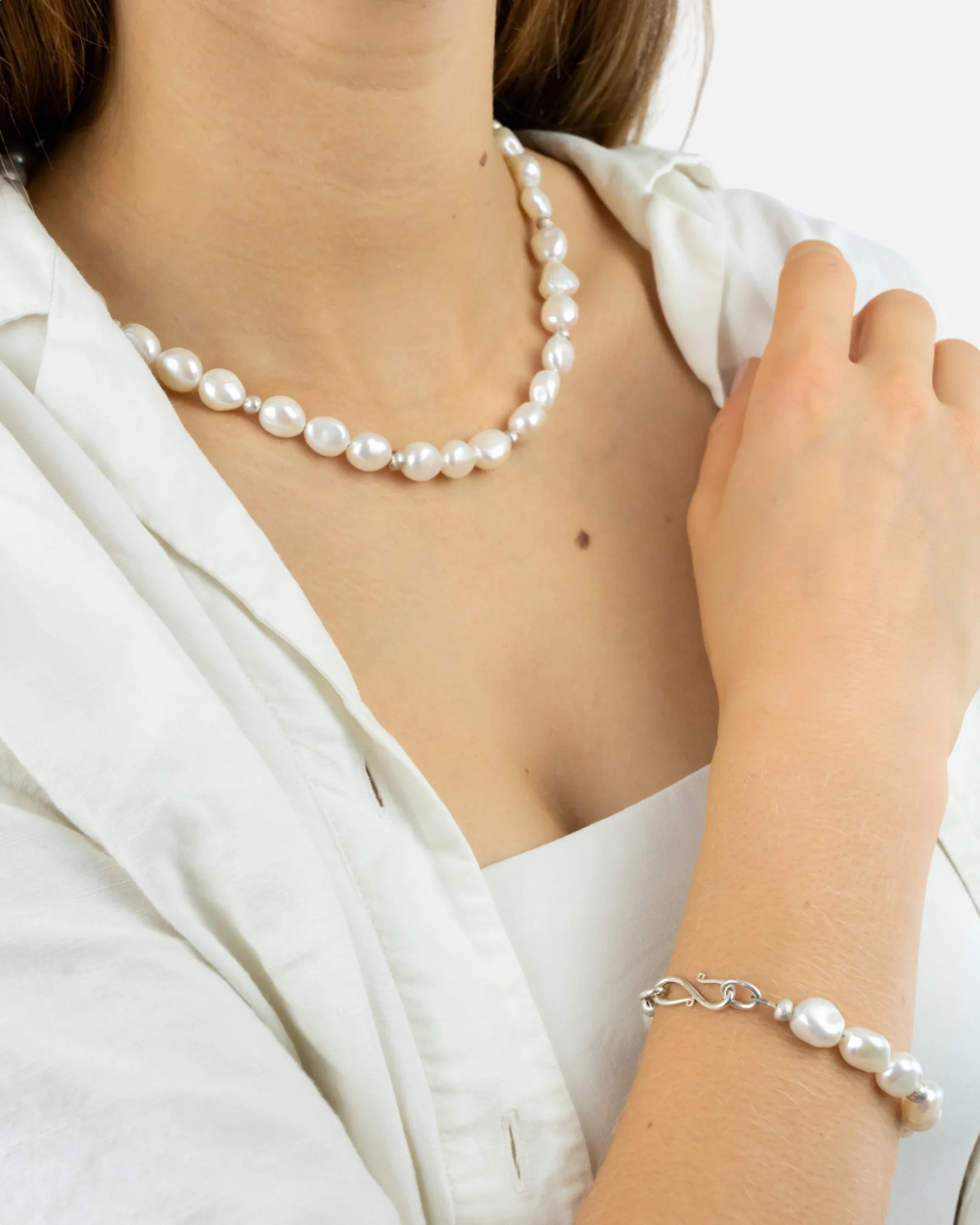 Woman wearing freshwater pearl necklace and bracelet with organic shapes, white blouse
