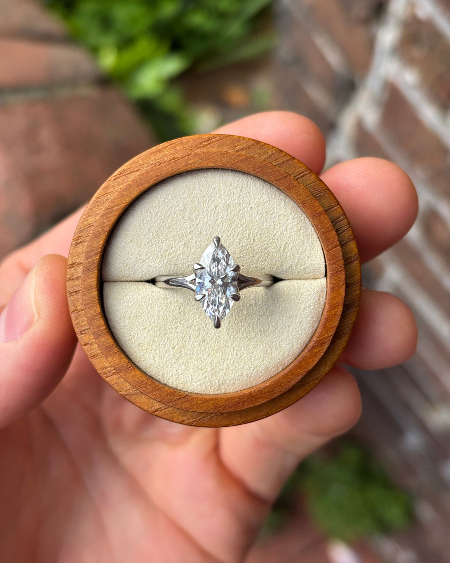 Marquise cut diamond engagement ring in a platinum tulip claw setting held in a round wooden box.