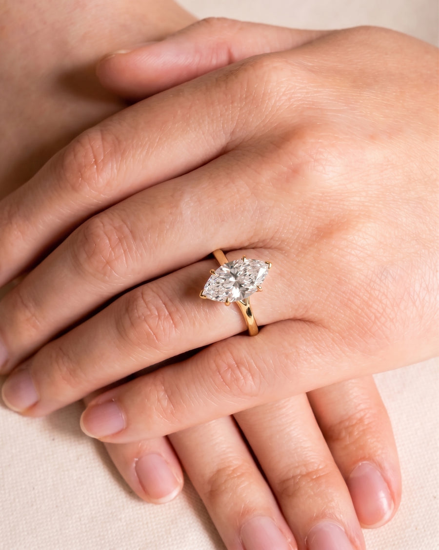 Marquise cut diamond engagement ring with a gold tulip claw setting worn on a finger.