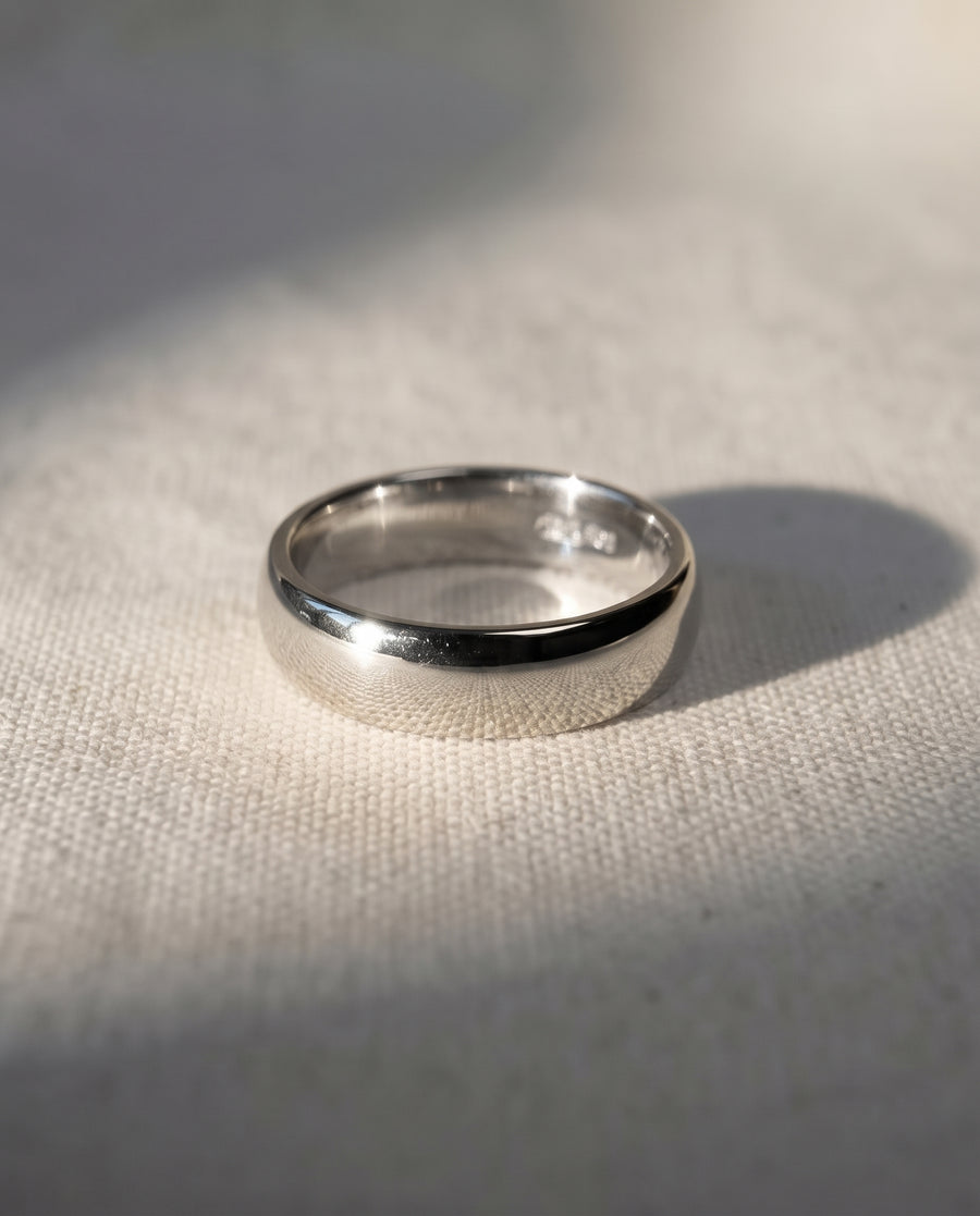 Polished 4mm platinum low court wedding ring with a smooth, rounded profile on a textured white surface.
