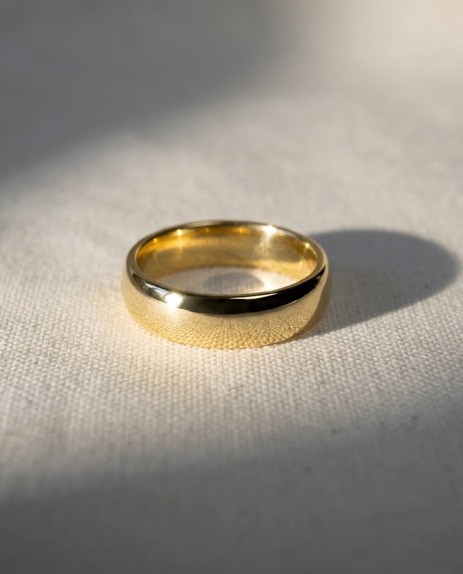4mm polished 9ct yellow gold low court wedding ring with a smooth, rounded profile on a textured fabric surface.
