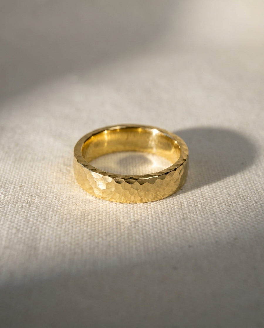 Flat gold wedding ring with a textured hammered finish resting on a light fabric surface.