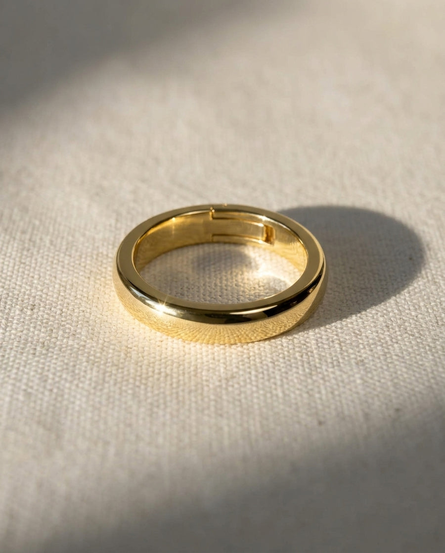 Polished gold hinged wedding band with a smooth, rounded design resting on a textured fabric surface.