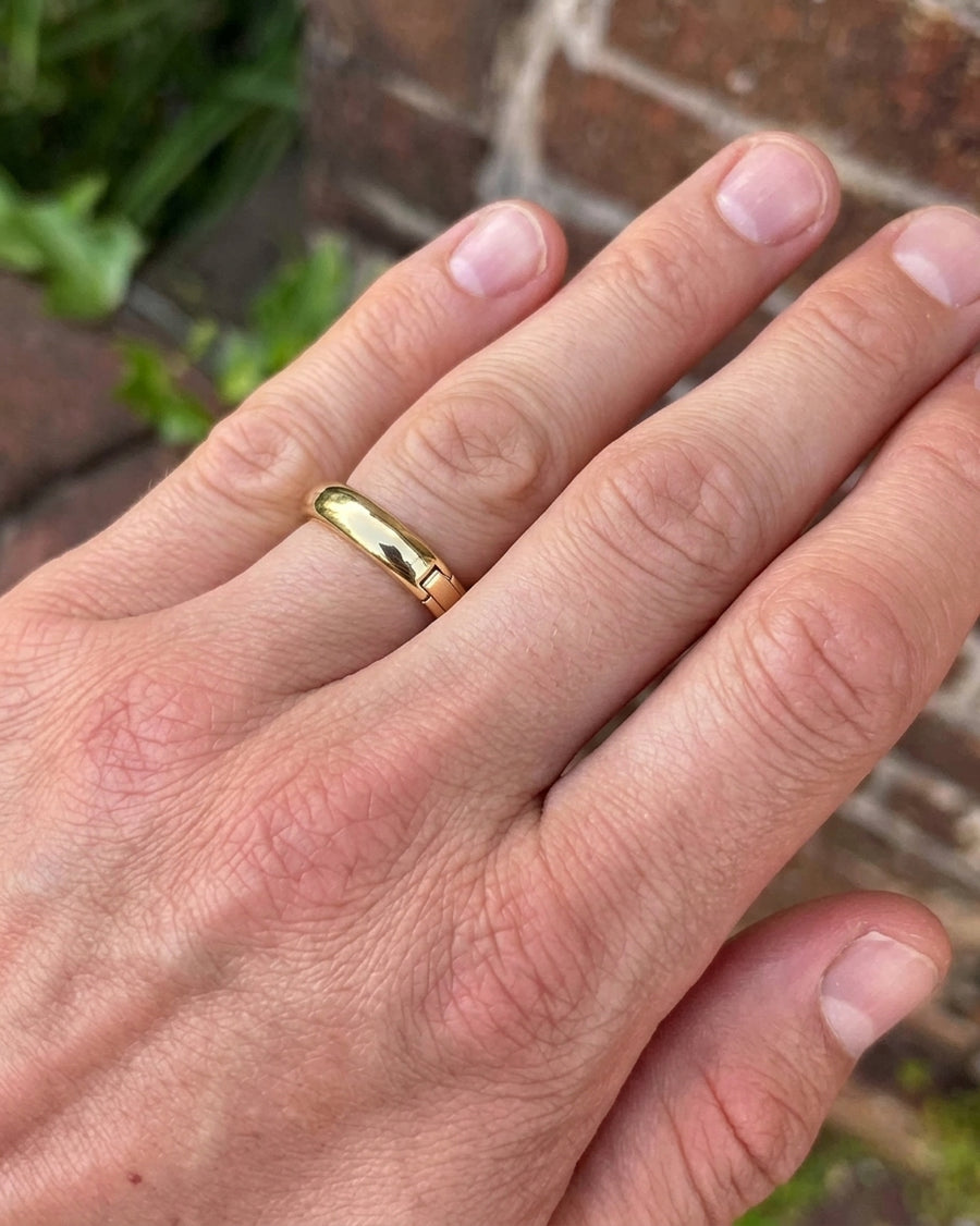 Polished gold hinged wedding band worn on a finger, featuring a smooth, rounded design with a visible side hinge.