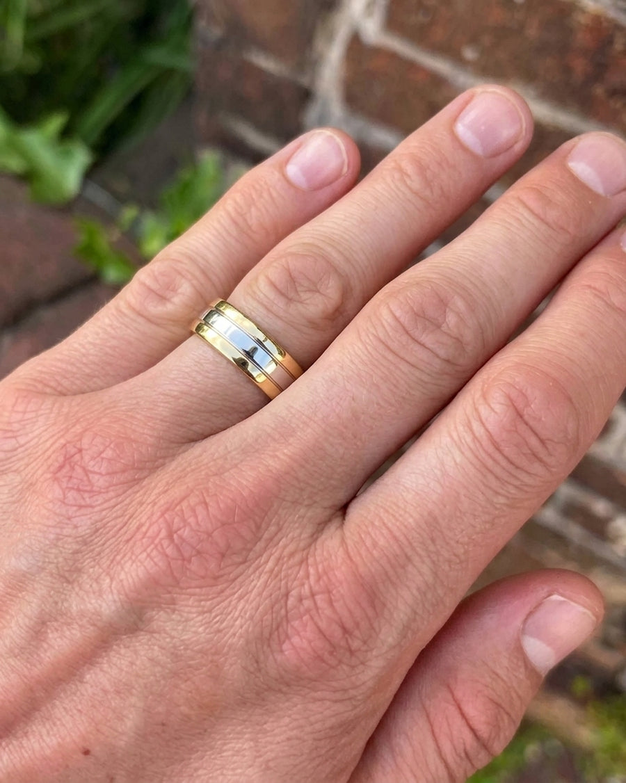 Flat wedding band featuring a silver-tone center stripe flanked by yellow gold edges worn on a finger.