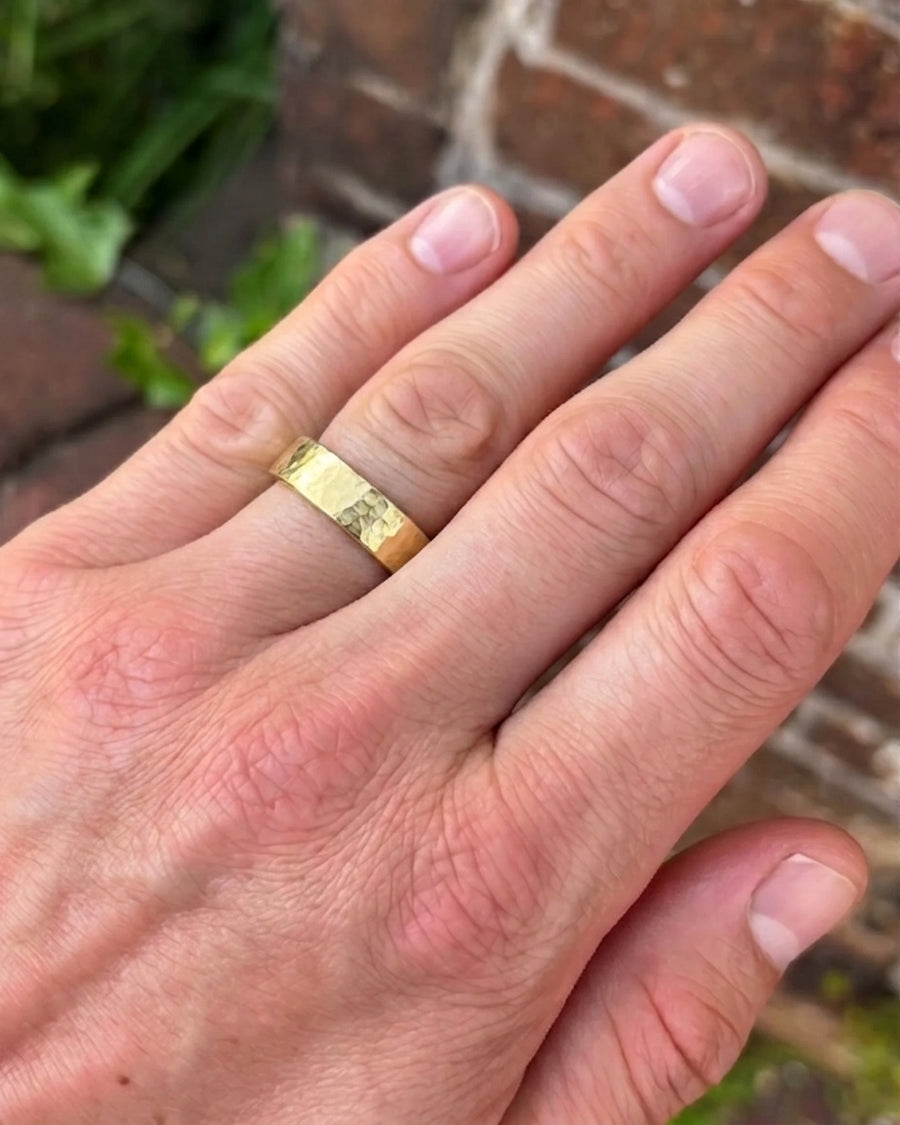 Gold wedding ring with a hammered texture worn on a man's finger.