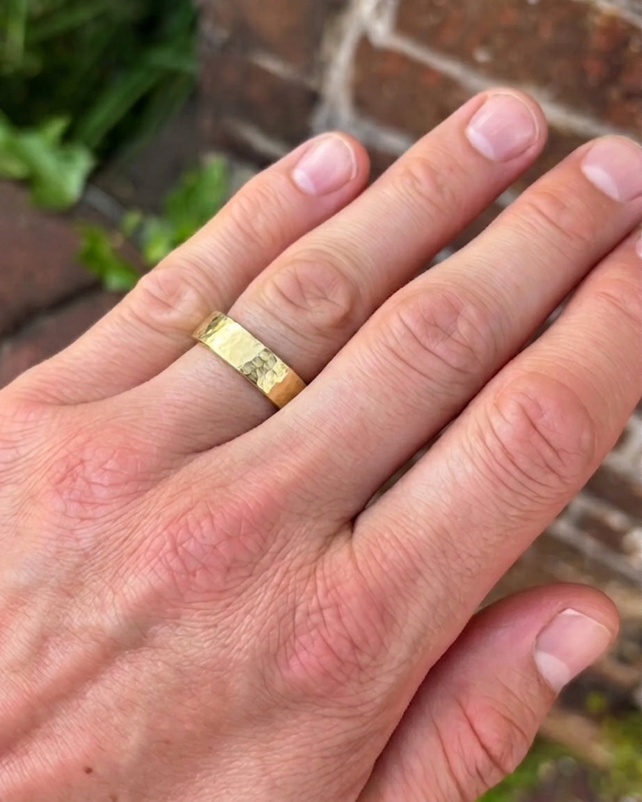 Gold wedding ring with a hammered texture worn on a man's finger.