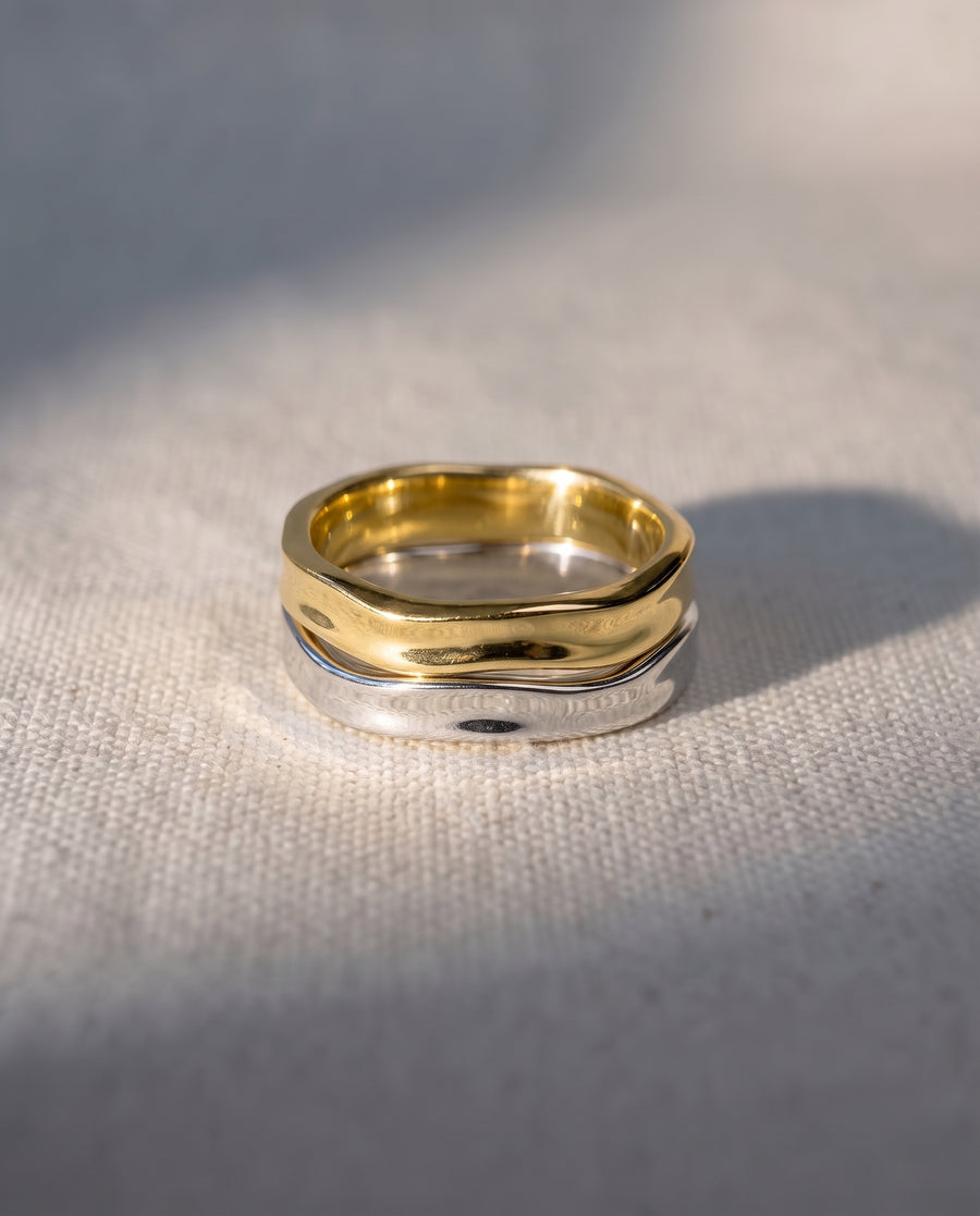 Two-tone mixed metal ring with a hammered, wavy design in gold and silver on a textured fabric background.
