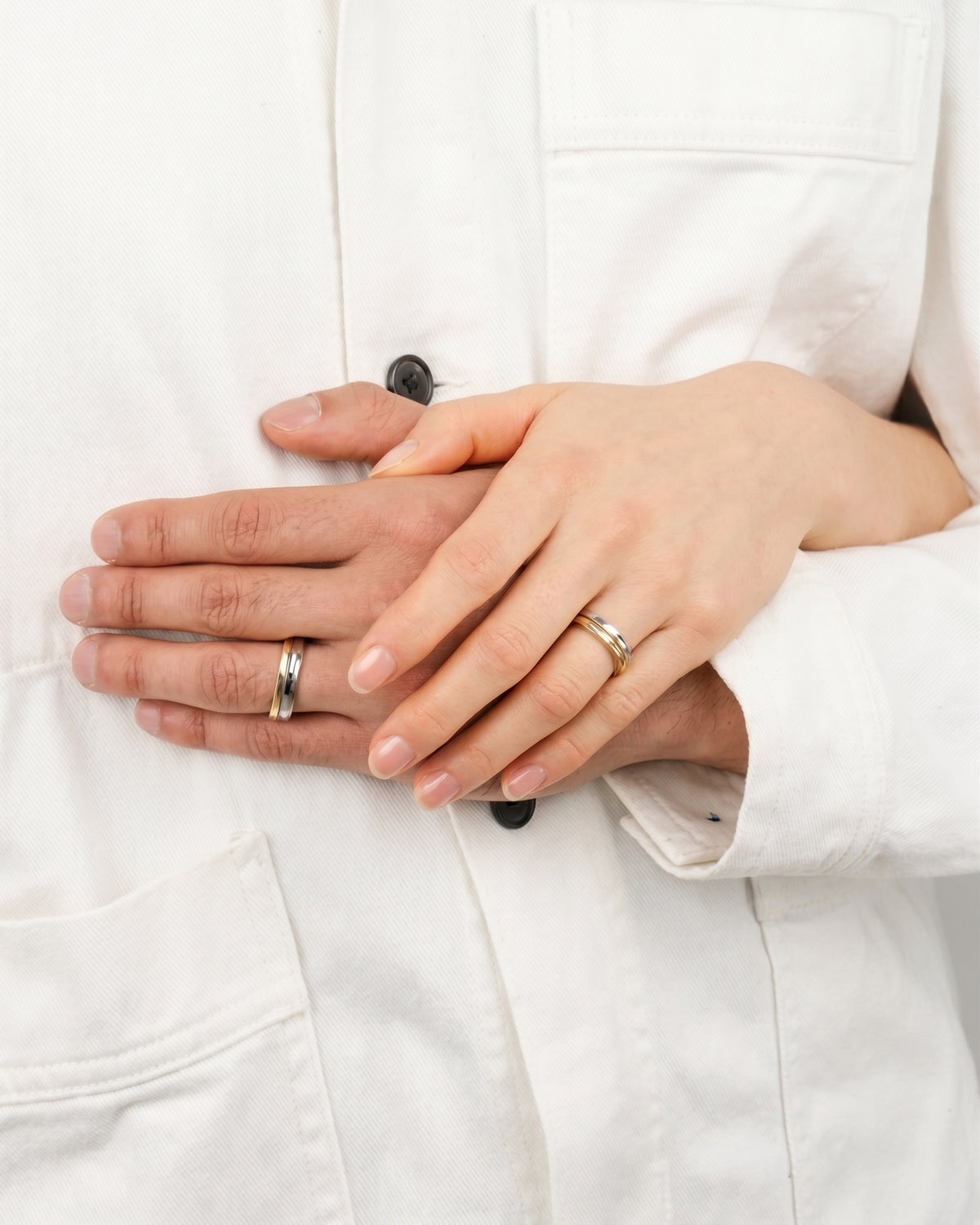 Two hands wearing matching mixed metal bands with gold and silver tones against a white shirt.