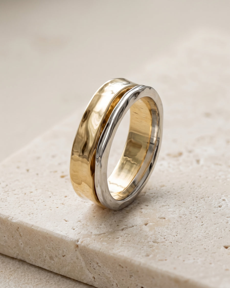 Two-tone wedding ring featuring a hammered gold band layered with a smooth silver band on a stone surface.