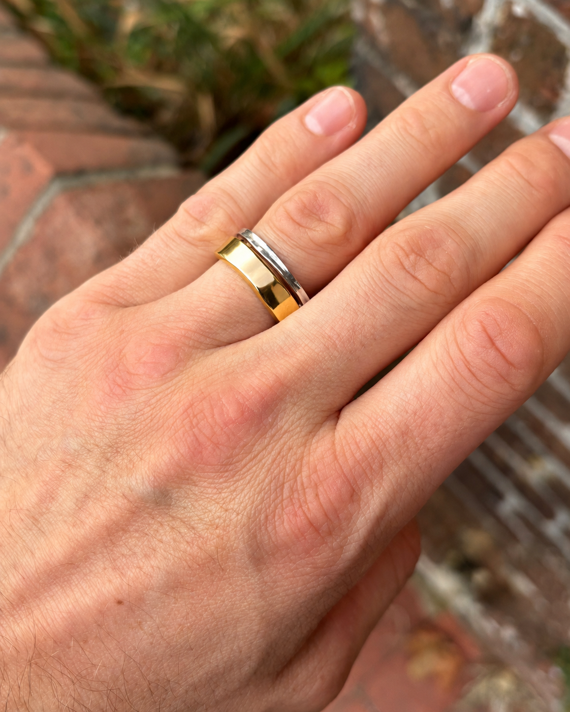 Two-tone wedding ring featuring a wide gold band and a thinner silver band worn on a finger.