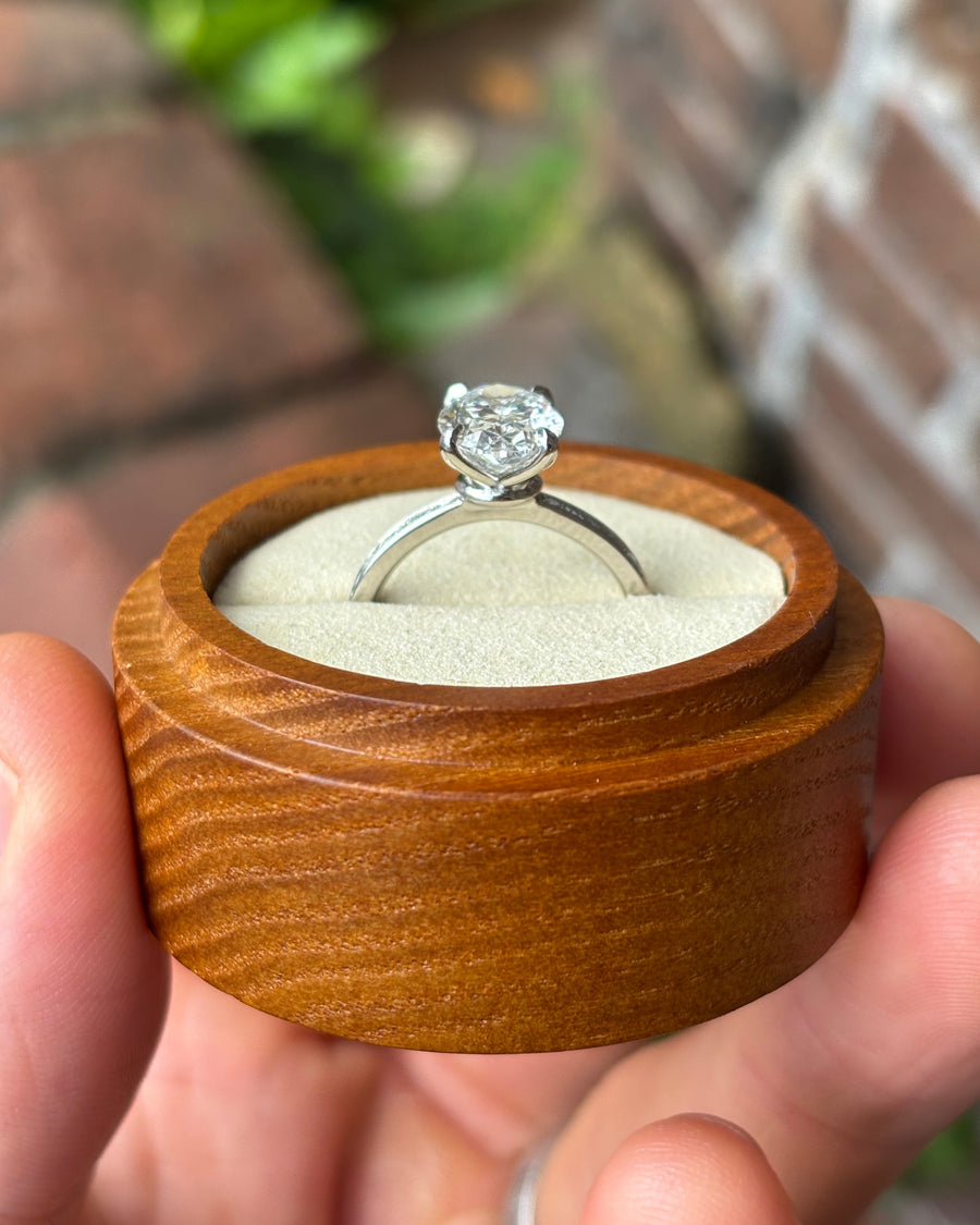 Oval lab diamond solitaire engagement ring with a pavé band in a wooden ring box.