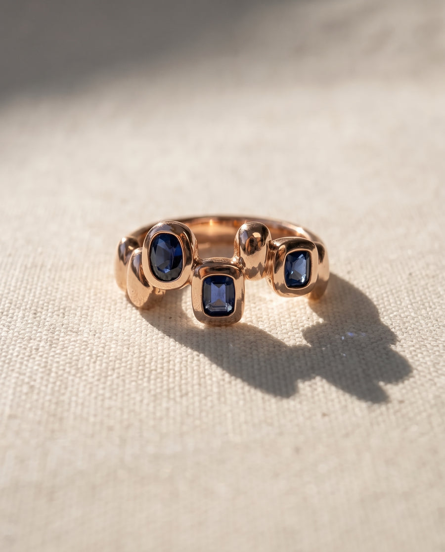 9ct rose gold eternity ring featuring three bezel-set blue sapphire gemstones in an organic pebble-shaped design.