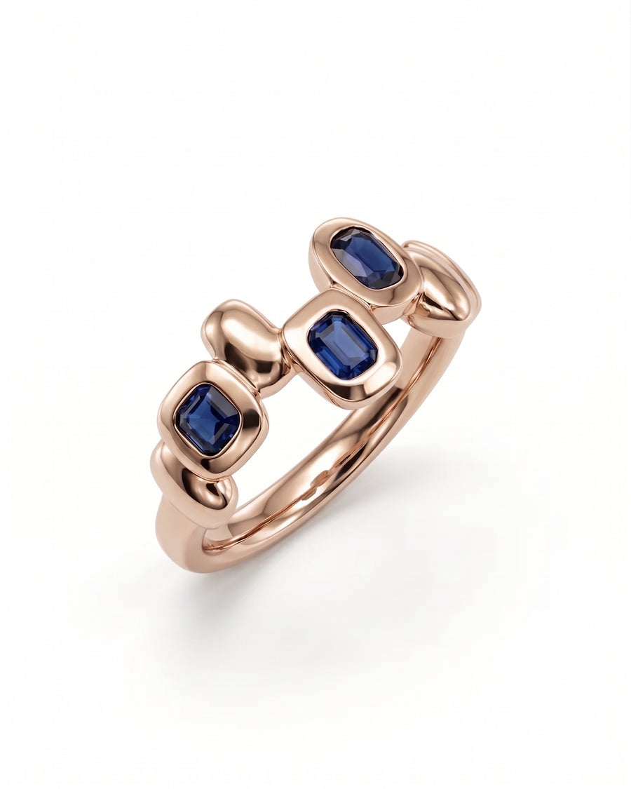 Rose gold eternity ring featuring three bezel-set rectangular blue sapphires in a smooth, pebble-like design.