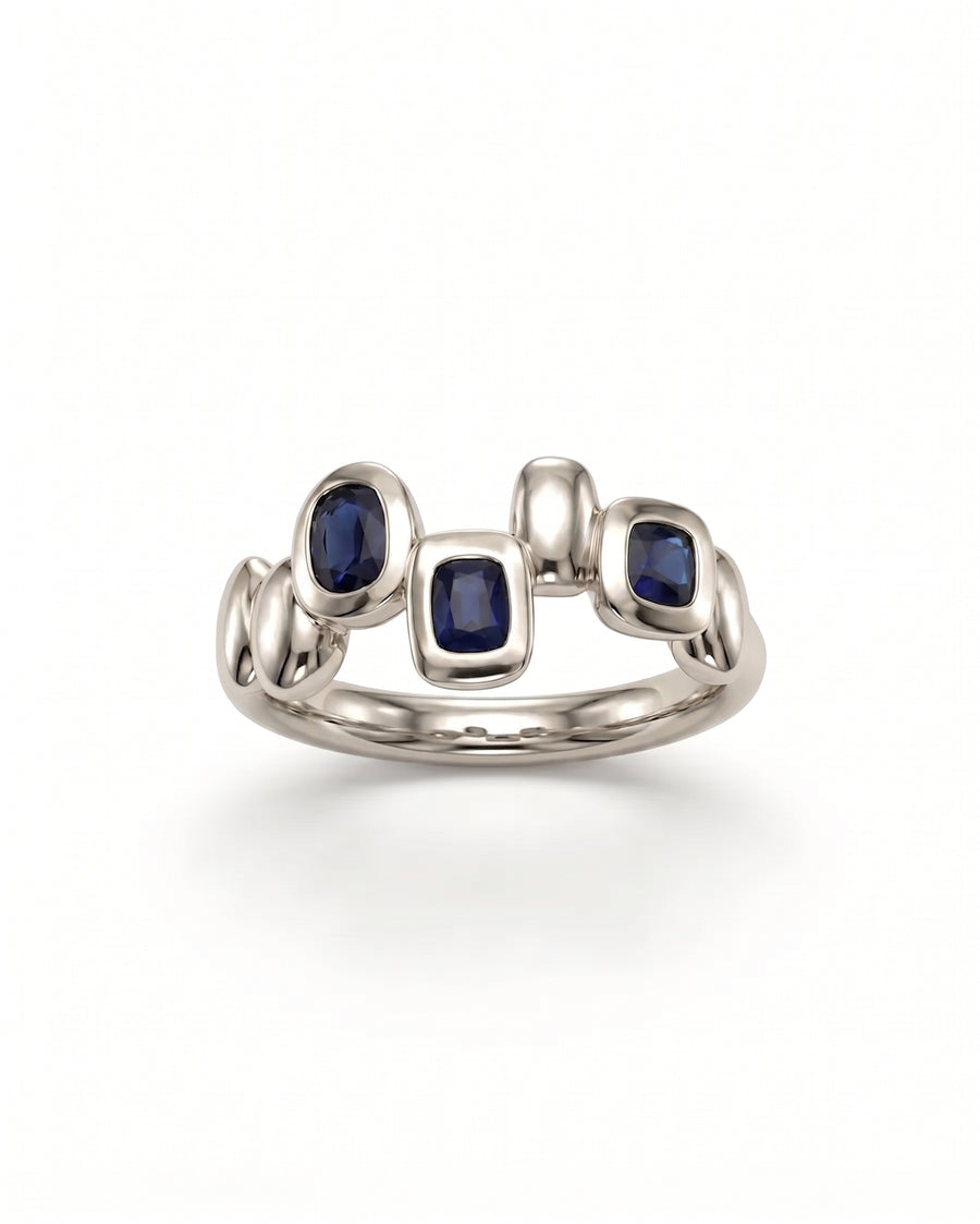 Silver eternity ring featuring organic pebble-shaped metal settings with three embedded blue sapphire gemstones.