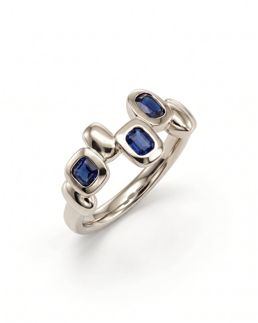 Silver eternity ring featuring three bezel-set blue sapphire gemstones in a smooth, pebble-inspired metal design.