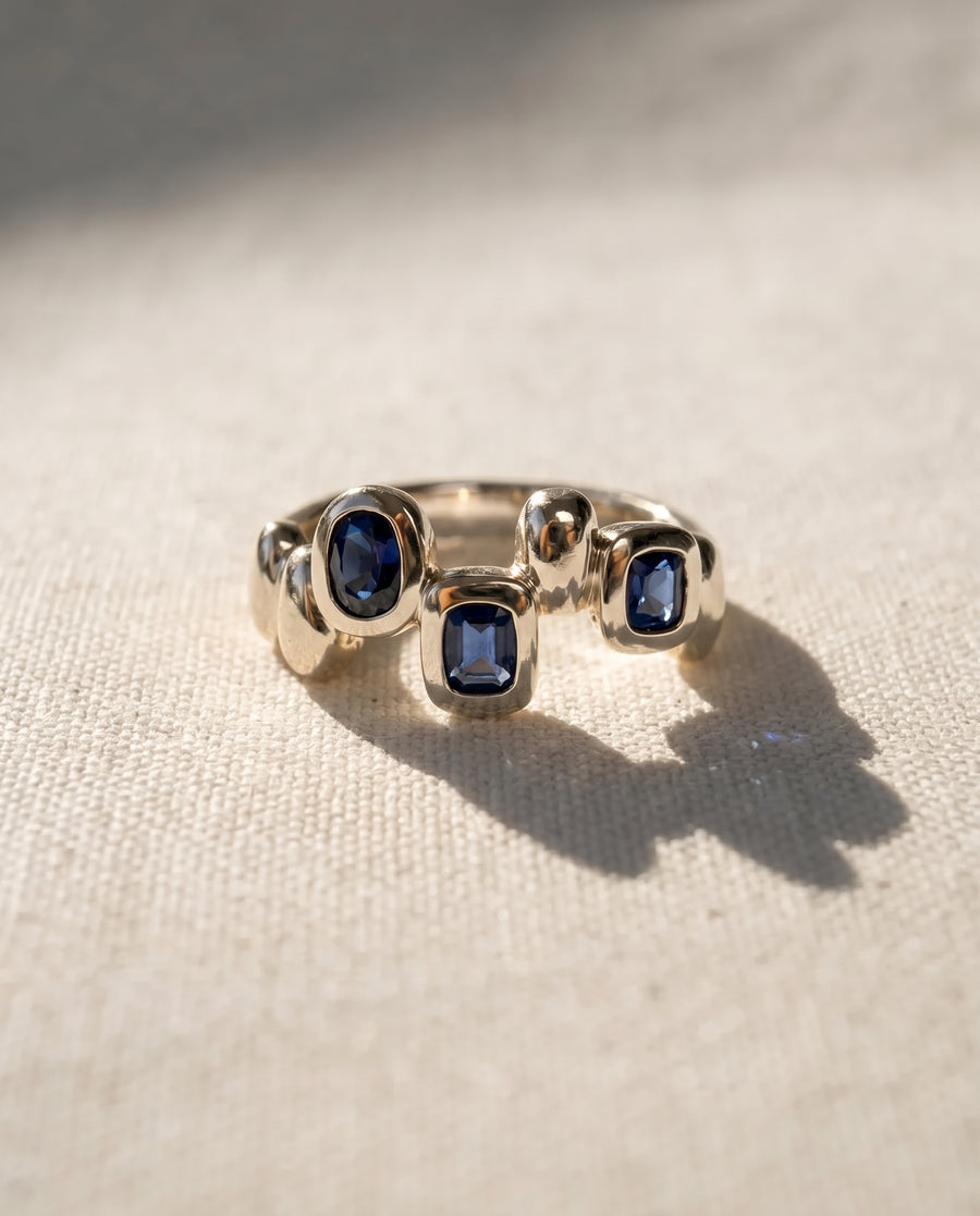 9ct white gold eternity ring featuring three bezel-set blue sapphires in an organic pebble-style design.
