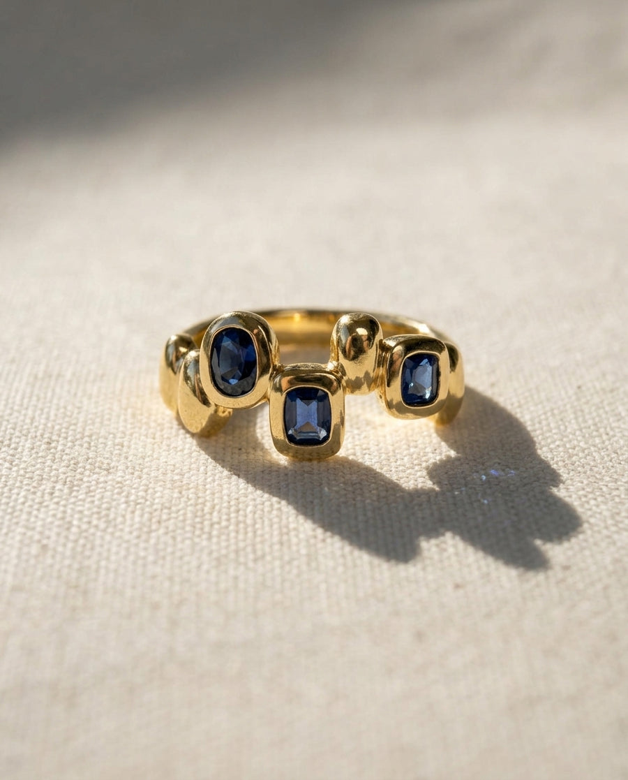 9ct yellow gold eternity ring featuring three bezel-set blue sapphires in an organic, pebble-inspired design.