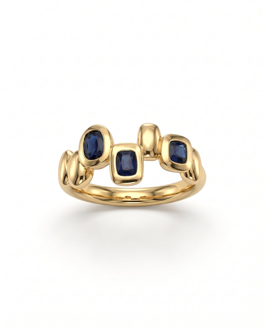 Gold eternity ring featuring three bezel-set blue sapphire gemstones in an organic pebble-shaped design.