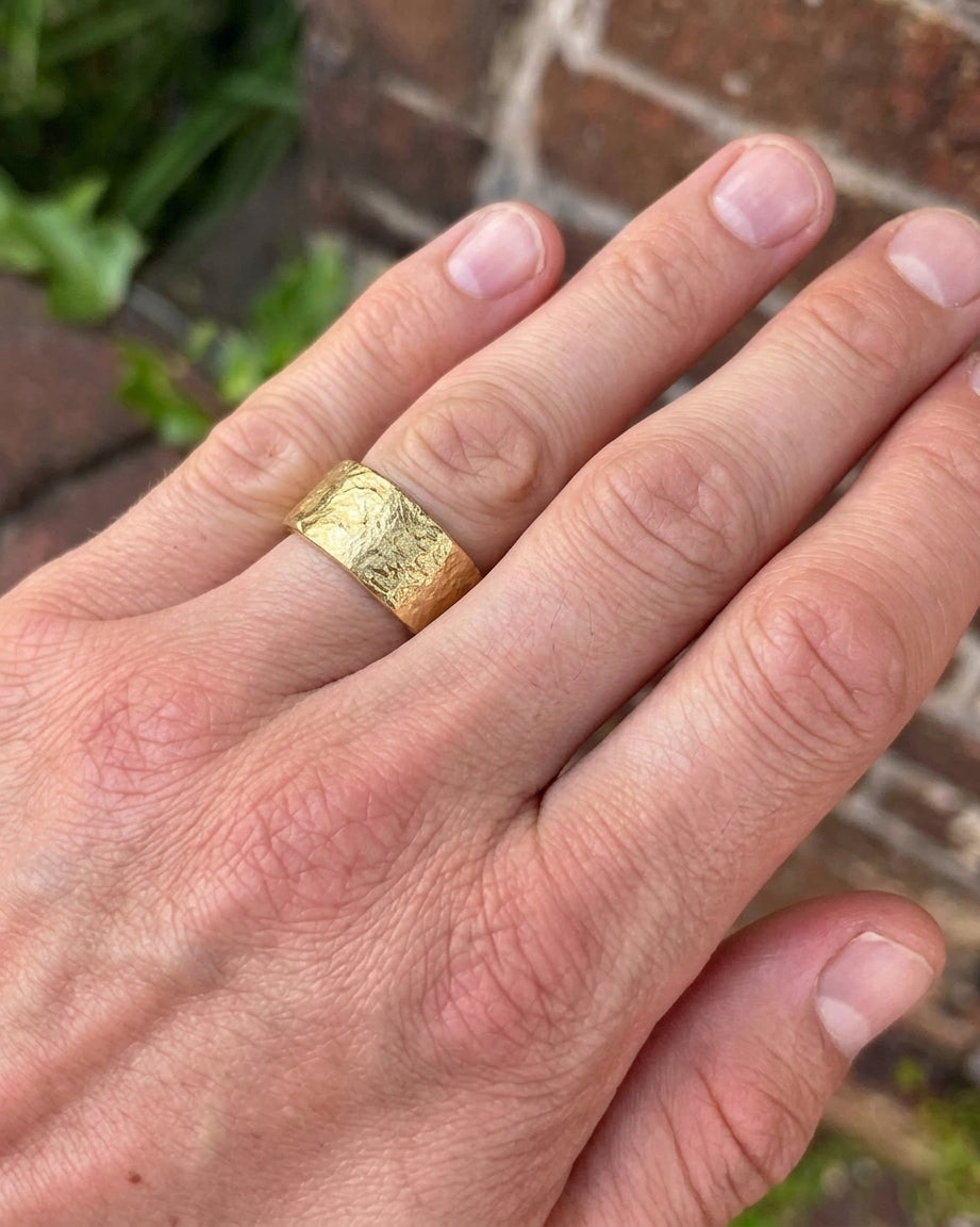 Wide gold wedding band with a textured, reticulated surface worn on a finger.