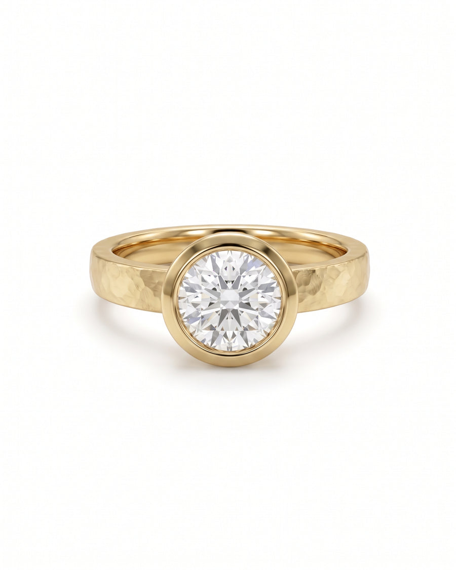 Round brilliant cut diamond engagement ring in a yellow gold band with a hammered bezel setting.