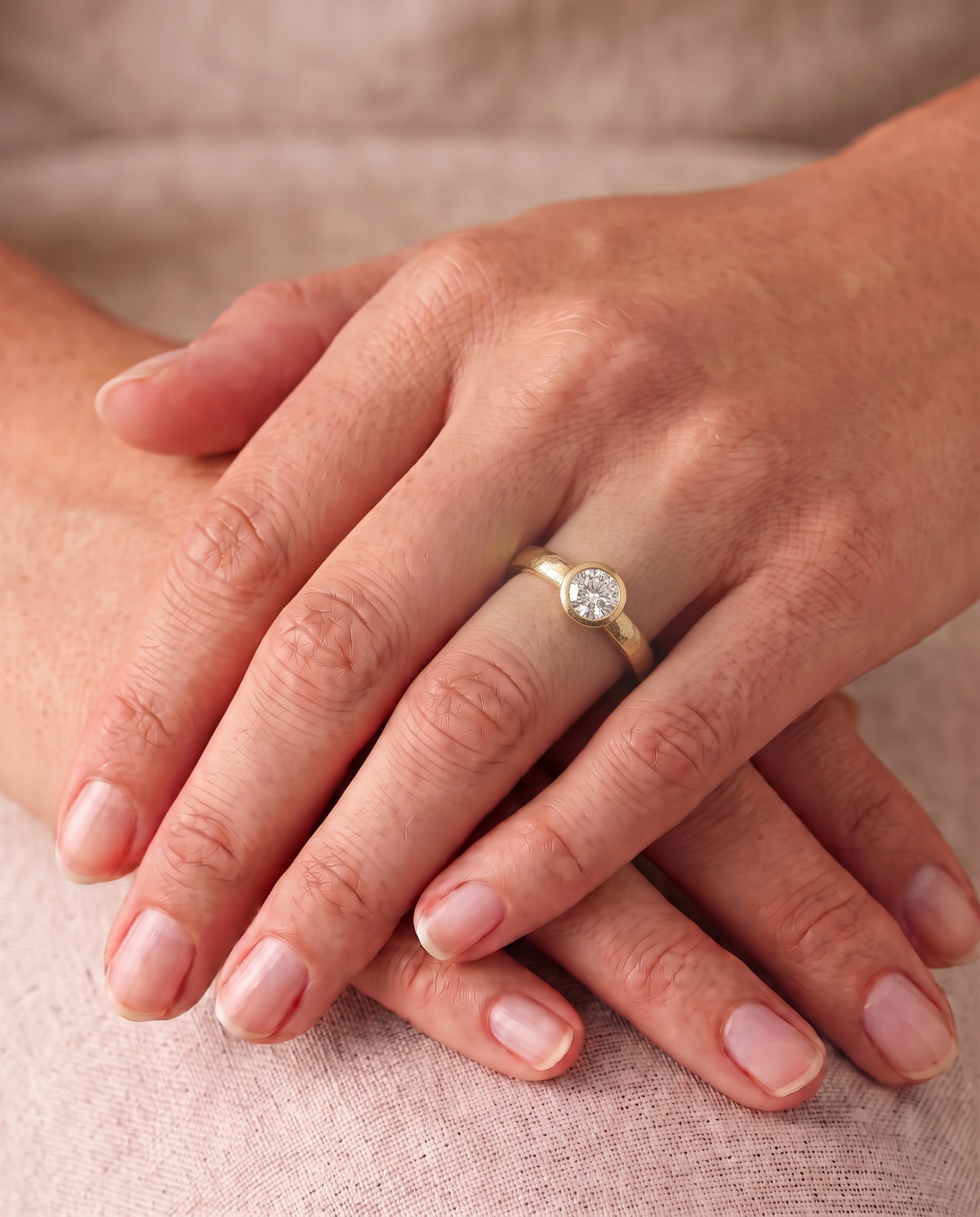 Round brilliant cut diamond engagement ring with a hammered gold bezel setting on a finger.