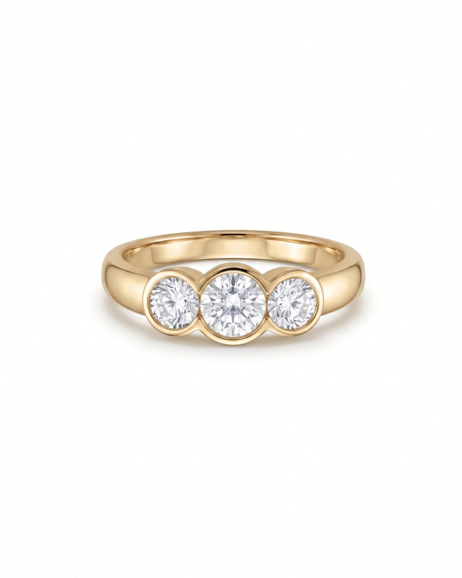 Yellow gold trilogy engagement ring featuring three bezel-set round cut diamonds.