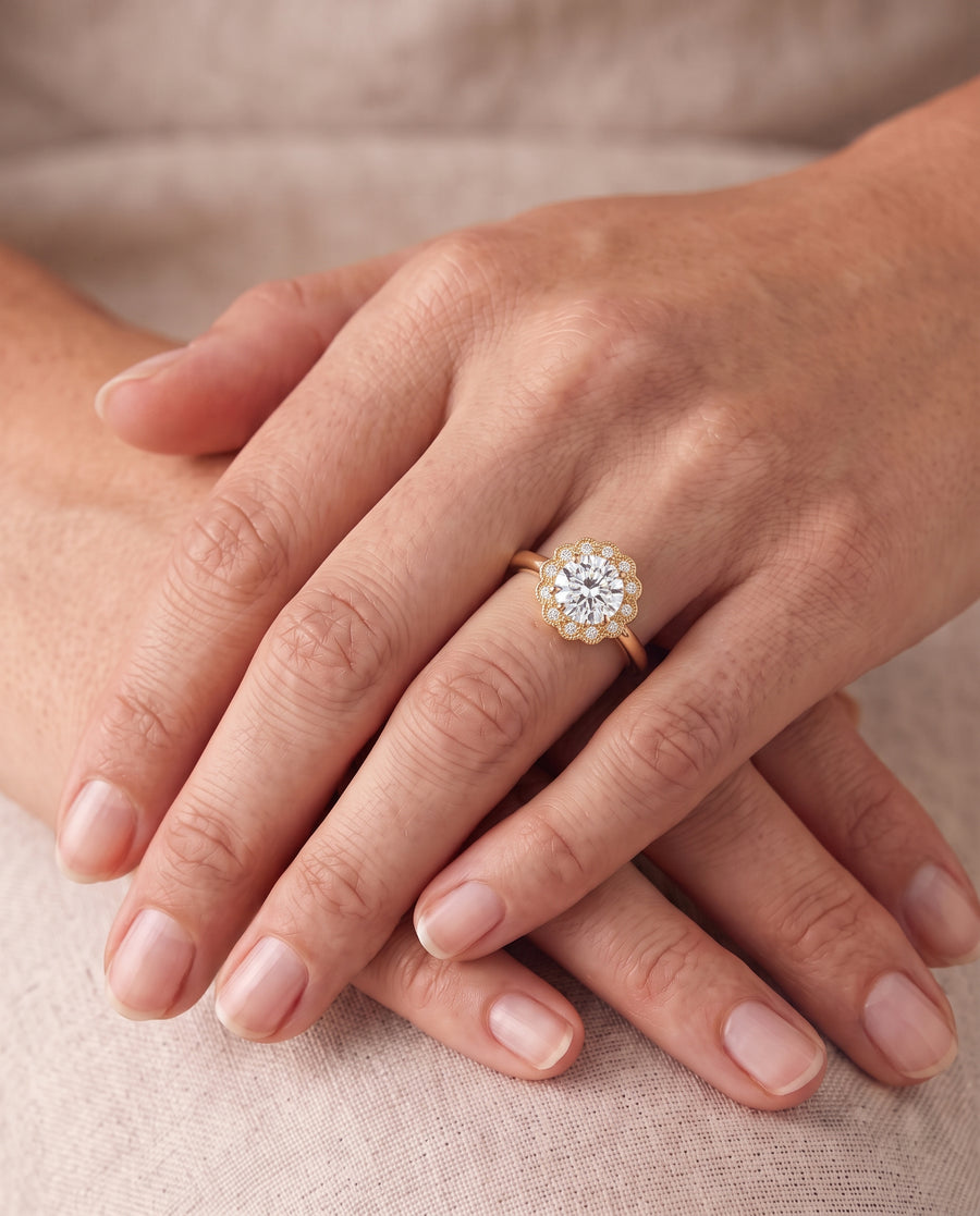 Gold engagement ring with a round diamond center stone in a scalloped cluster setting on a finger.