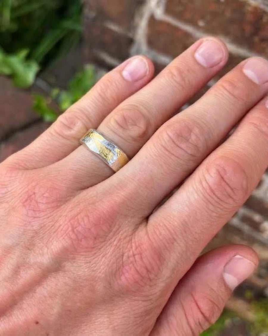 Flat ring featuring a hammered silver and gold mixed metal band worn on a finger.