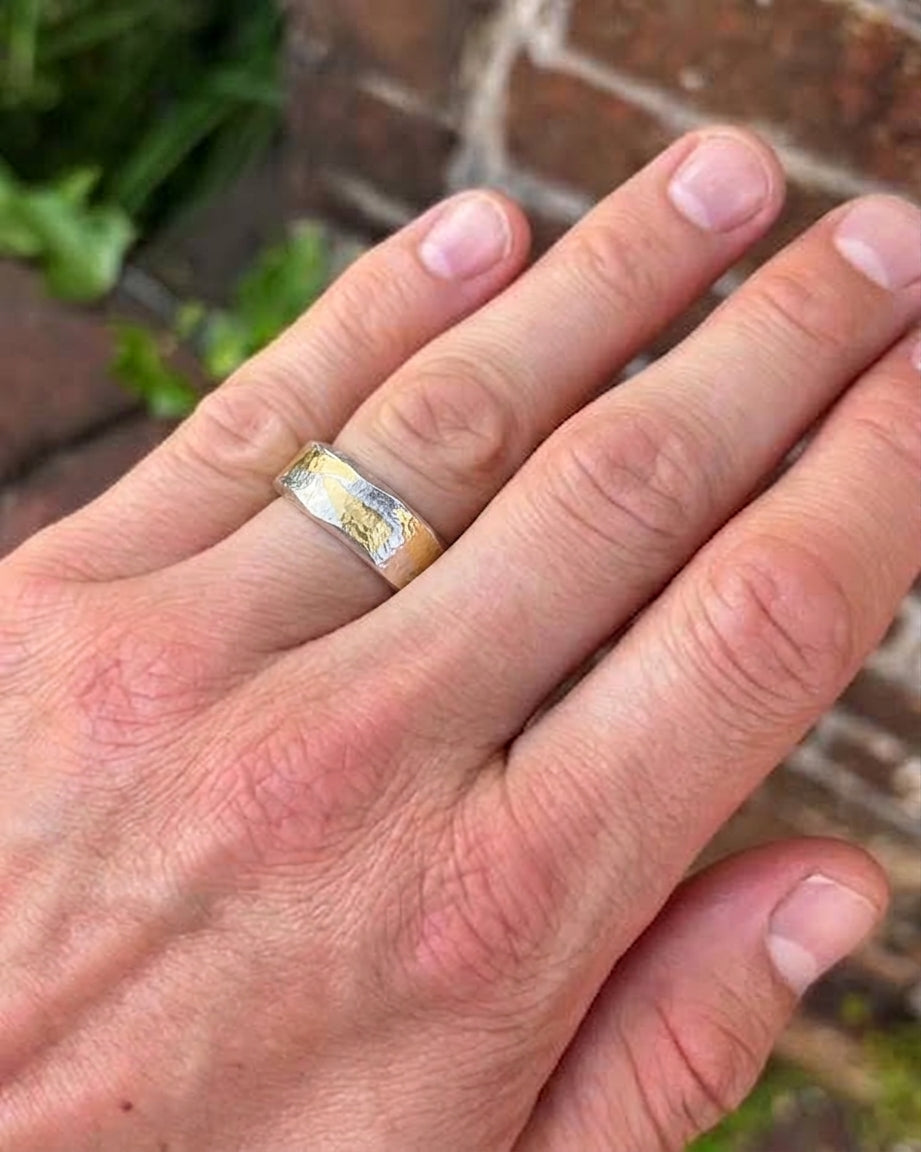 Flat ring featuring a hammered silver and gold mixed metal band worn on a finger.