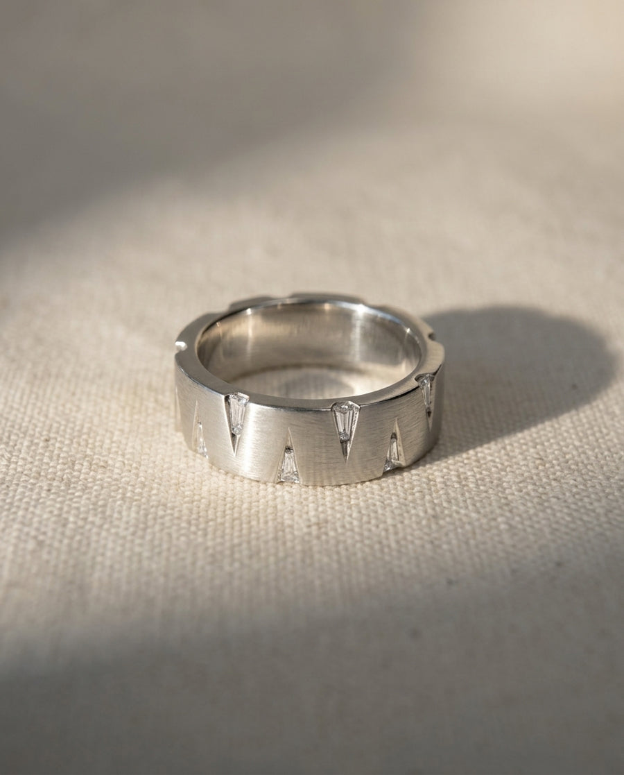Brushed platinum band ring featuring V-shaped cutouts with inset baguette diamonds on a textured fabric background.