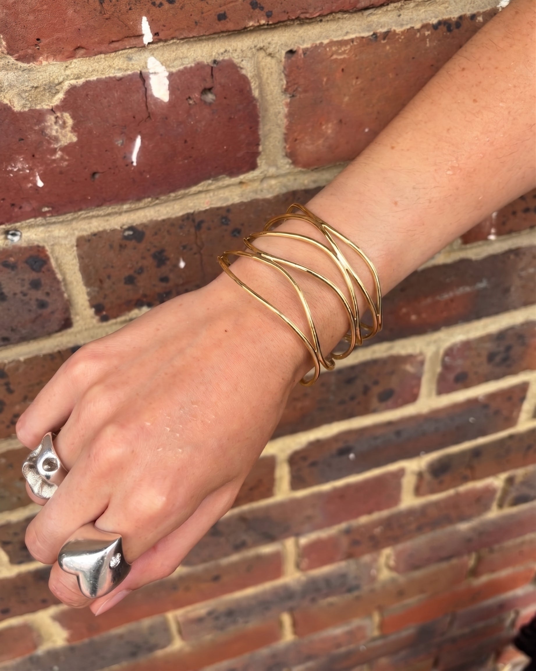 Wide six-strand solid 9ct gold cuff bangle worn on a wrist against a brick background.