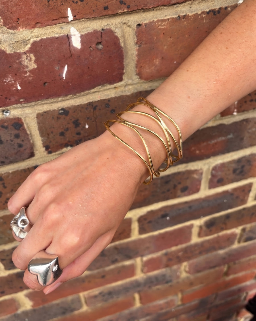 Wide six-strand solid 9ct gold cuff bangle worn on a wrist against a brick background.