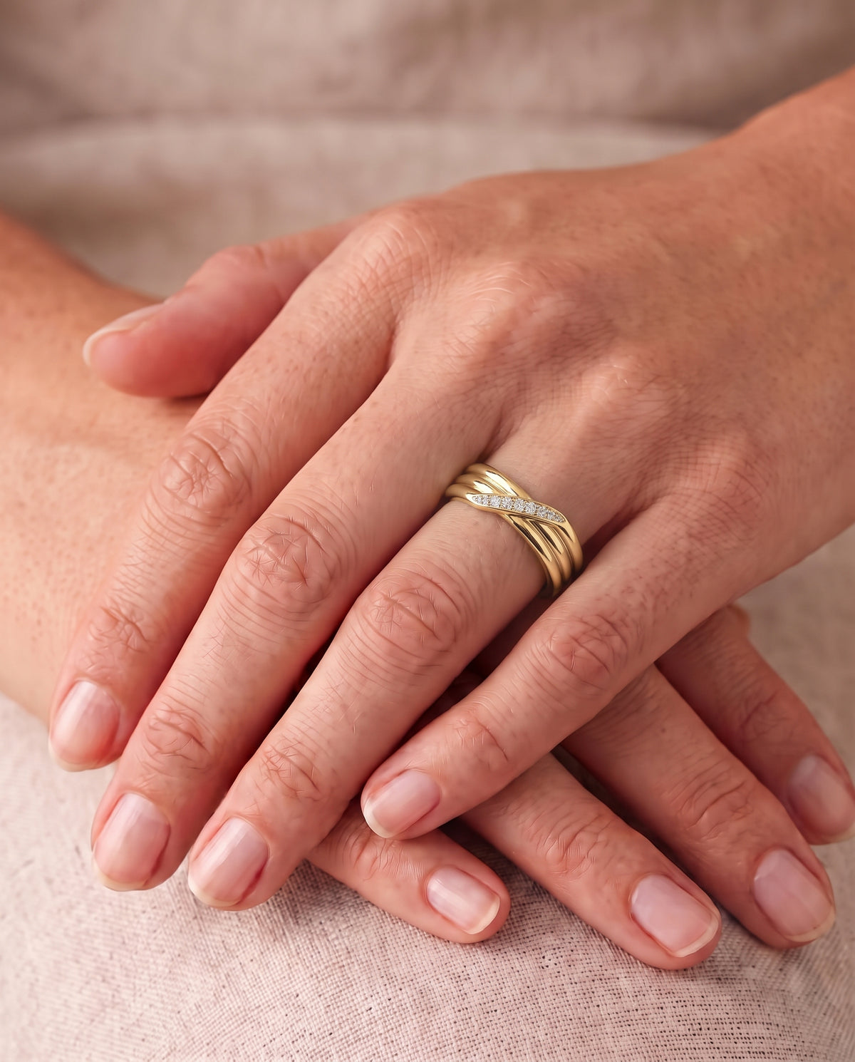 Gold three-strand crossover ring featuring a row of small diamonds on a finger.