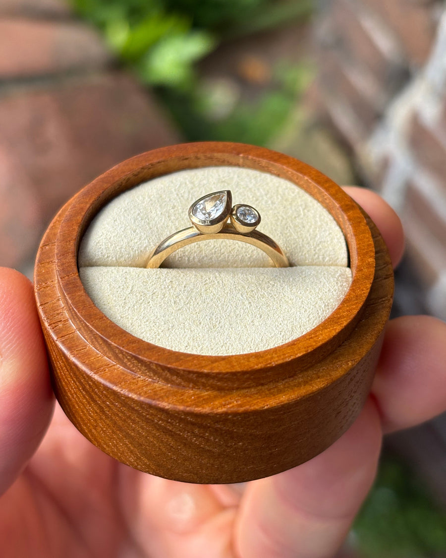 Gold toi et moi engagement ring with a pear and round diamond in bezel settings inside a wooden box.