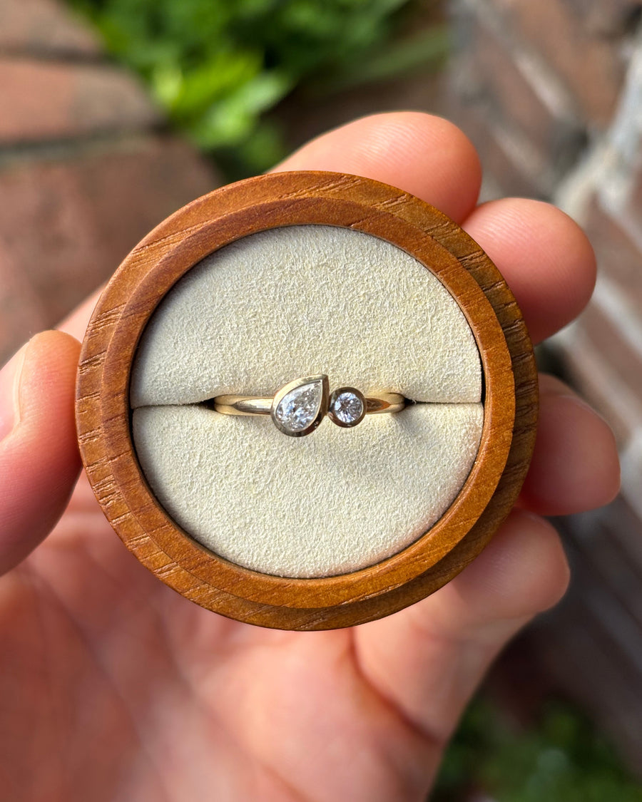 9ct yellow gold toi et moi engagement ring featuring a bezel-set pear and round diamond in a wooden box.