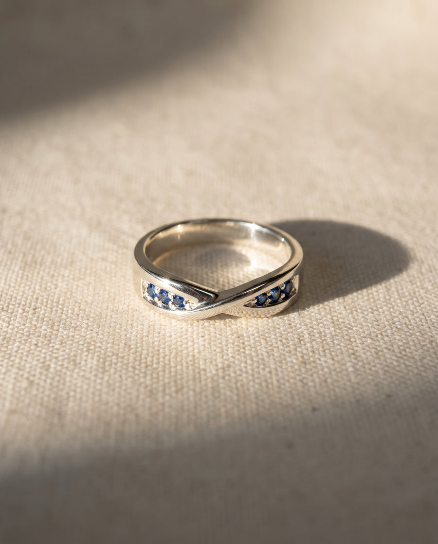 Silver twist ring featuring small blue sapphire gemstones set in a crossover band design.