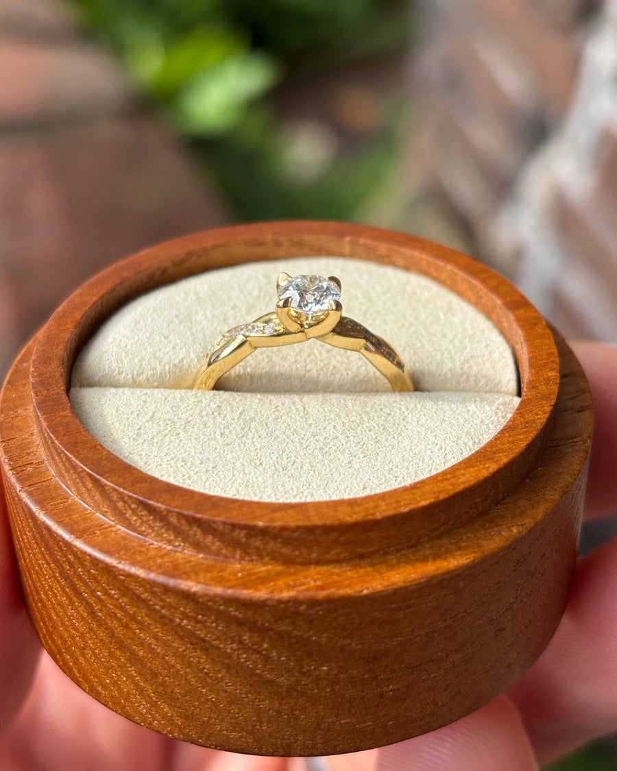 Round cut diamond engagement ring with a gold twist claw band in a wooden ring box.
