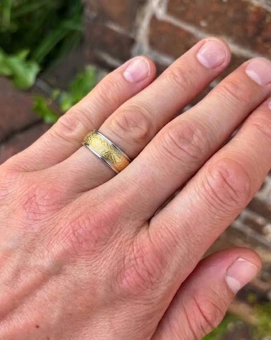Two-tone wedding band with a textured matte gold center and smooth silver edges worn on a finger.