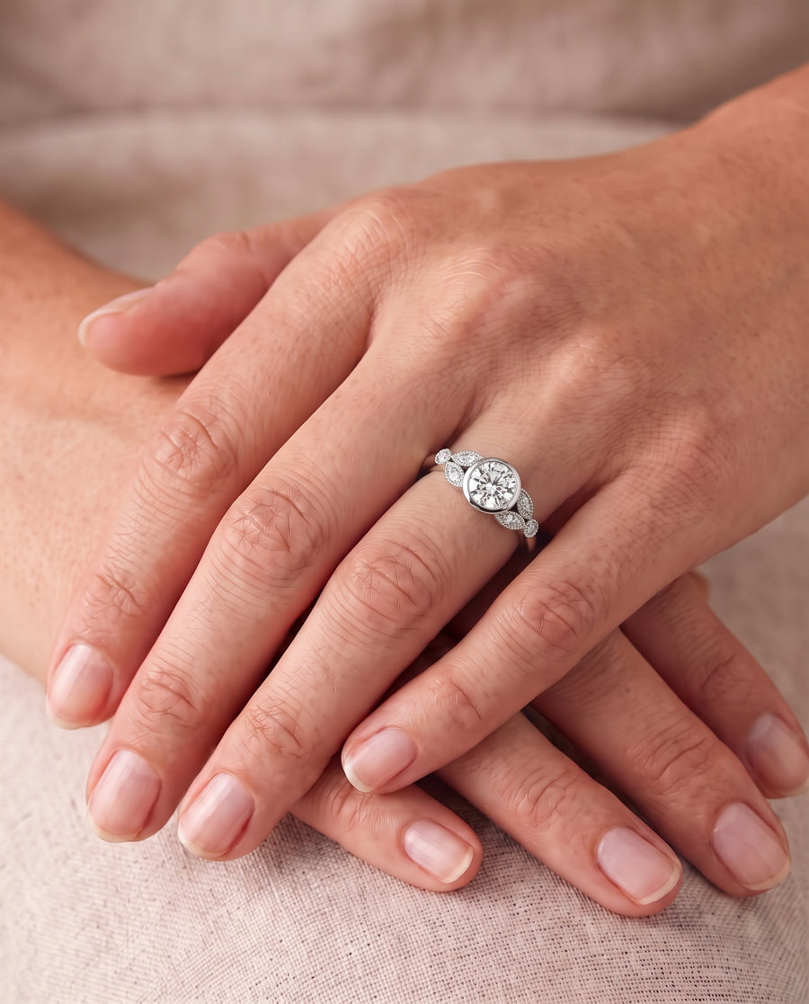 Round diamond engagement ring in a silver-tone bezel setting with accent stones on a platinum band.