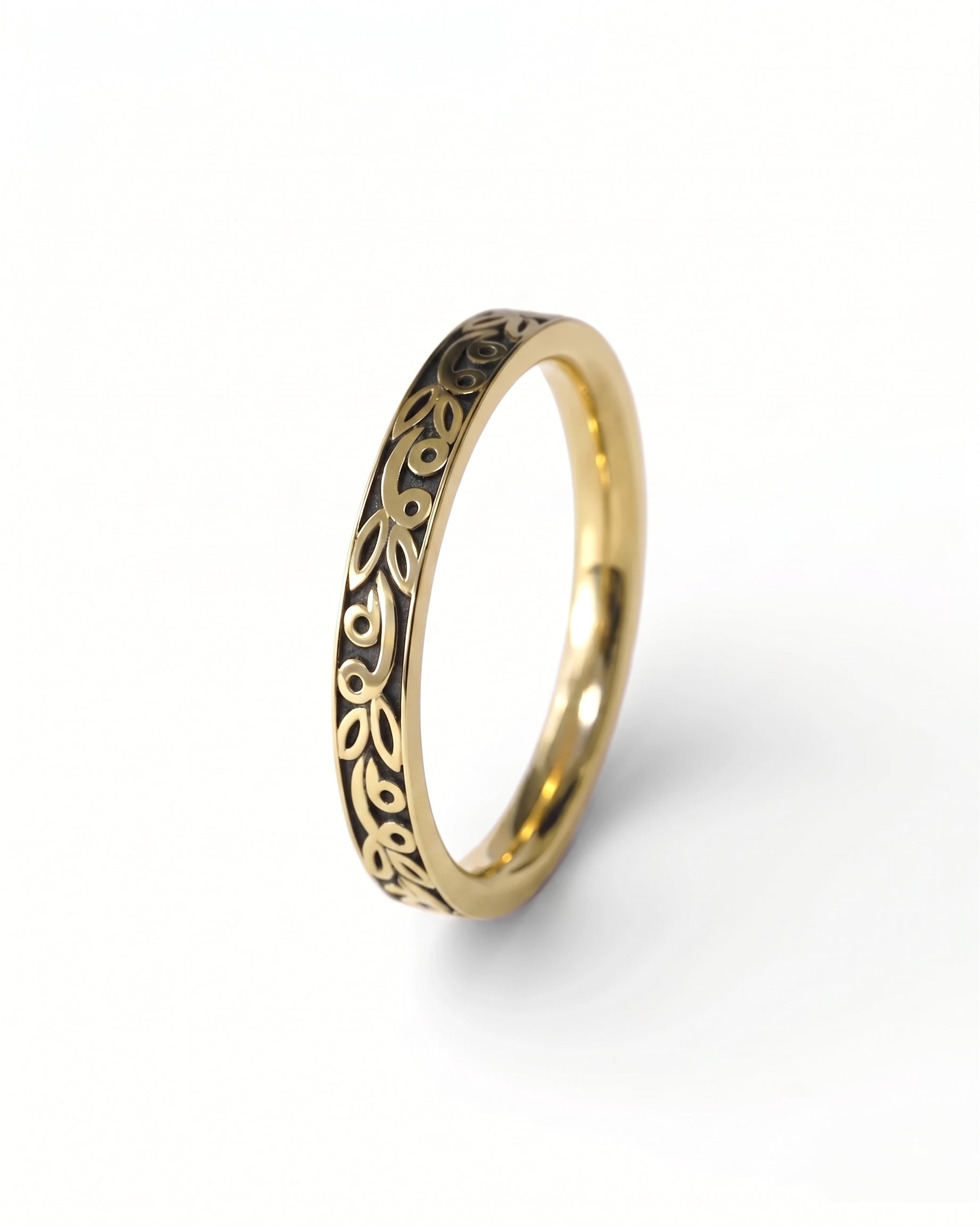 Gold wedding ring with a dark, carved leaf pattern along the outer band.