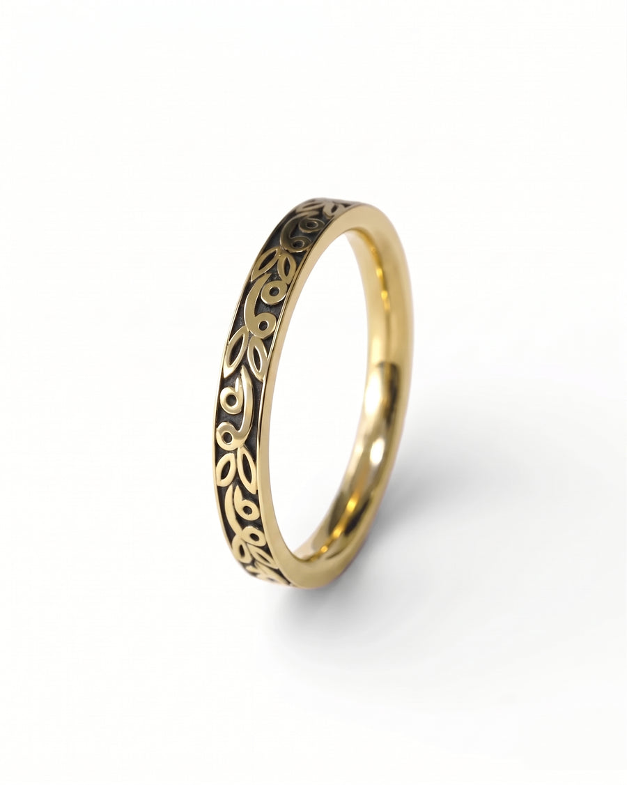 Gold wedding ring with a dark, carved leaf pattern along the outer band.