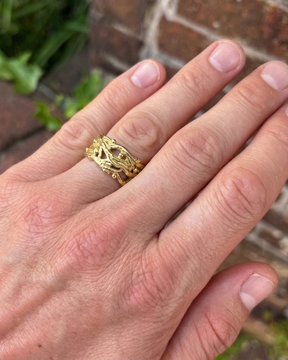 Wide gold ring with an organic, textured seaweed-inspired design worn on a finger.