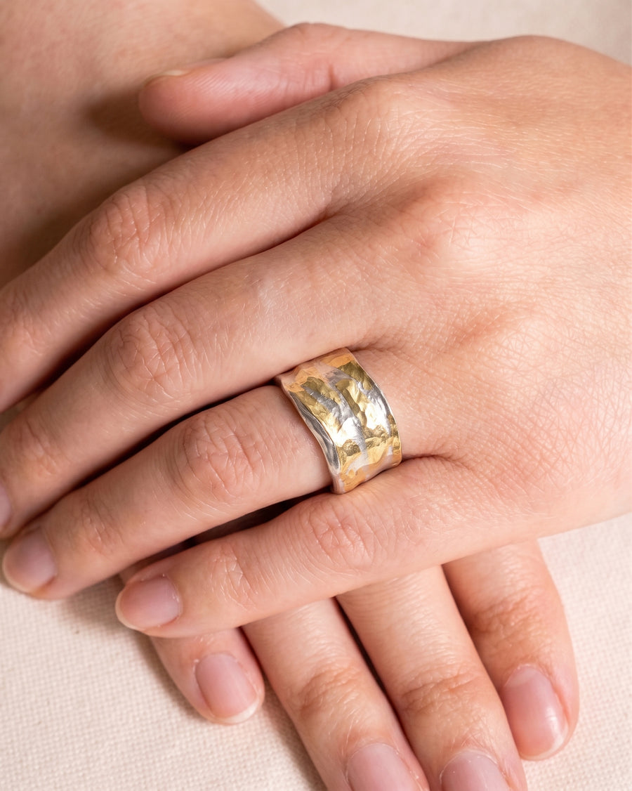 Wide band ring featuring a hammered gold center and silver edges worn on a finger.