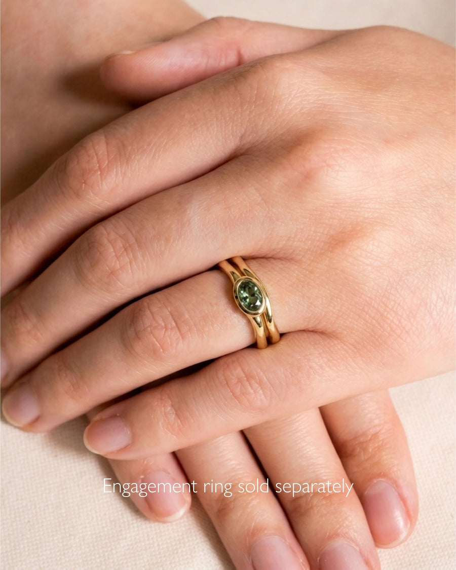 Gold wedding ring with an uneven, wavy band worn on a finger.
