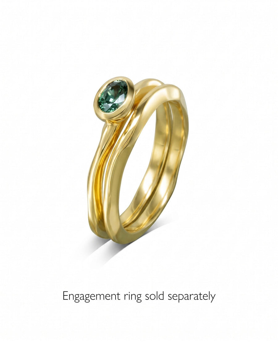 Gold wedding ring with an uneven, wavy band design and a bezel-set oval green gemstone.