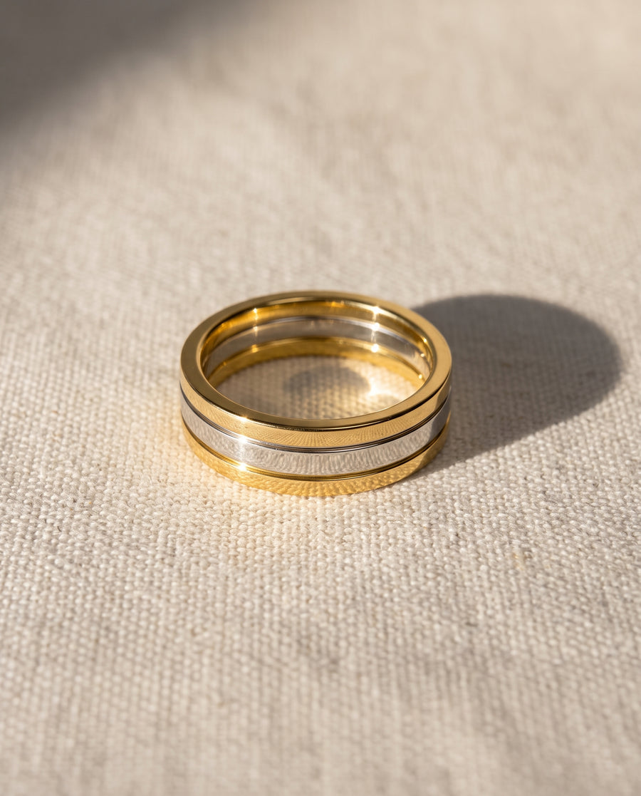 Flat wedding band featuring a silver-tone center stripe flanked by polished gold-tone metal edges.